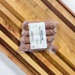 Vacuum-sealed package of sausages lying on a wooden diagonal slat table, with a label reading 'Whole Hog Sausage'