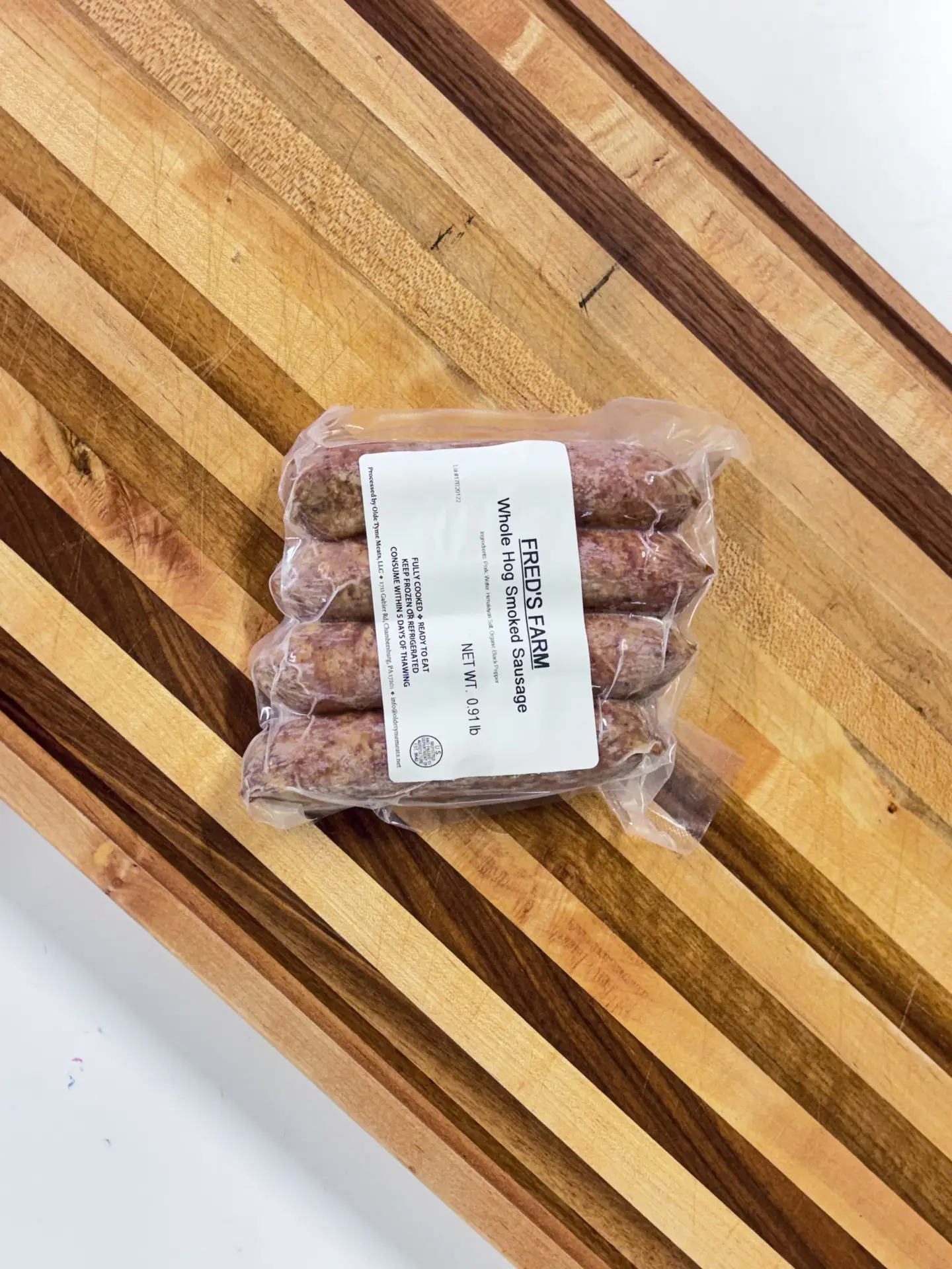 Vacuum-sealed package of sausages lying on a wooden diagonal slat table, with a label reading 'Whole Hog Sausage'