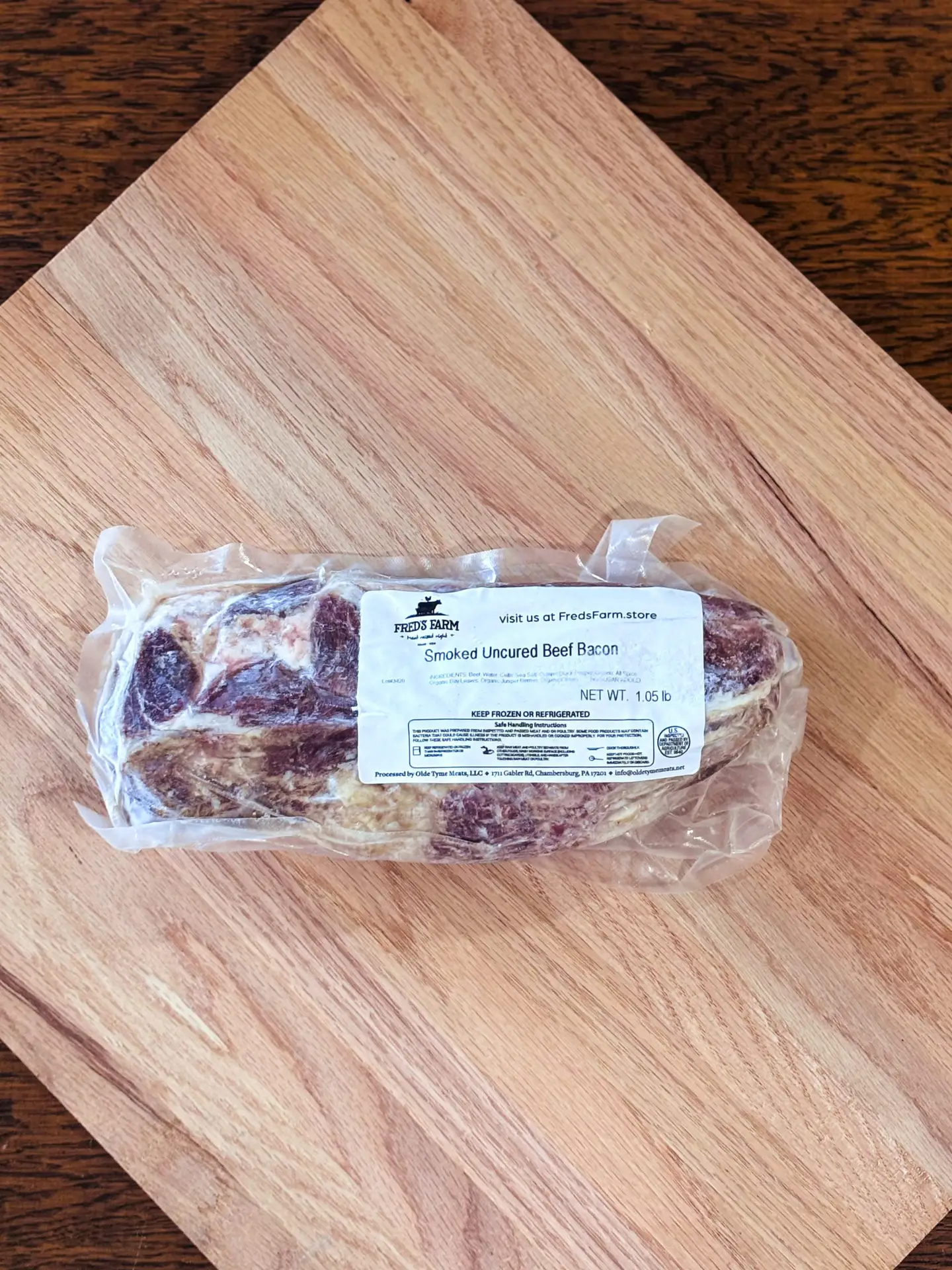 Vacuum-sealed smoked uncured beef bacon on a light wooden cutting board.