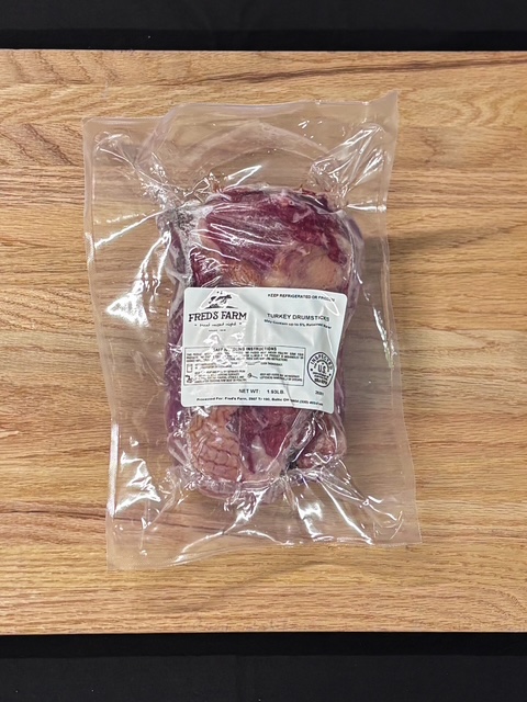 Vacuum-sealed package of turkey drumsticks labeled Fred's Farm on a wooden counter.